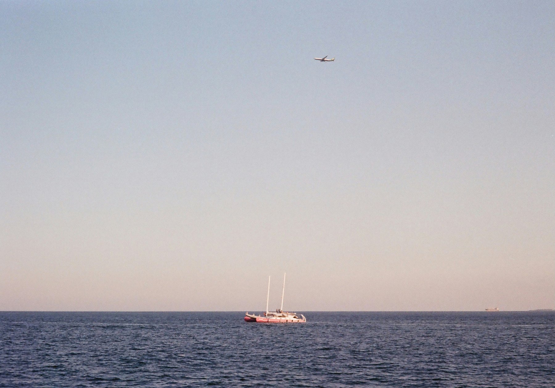 Catamaran at sea with an aircraft passing overhead